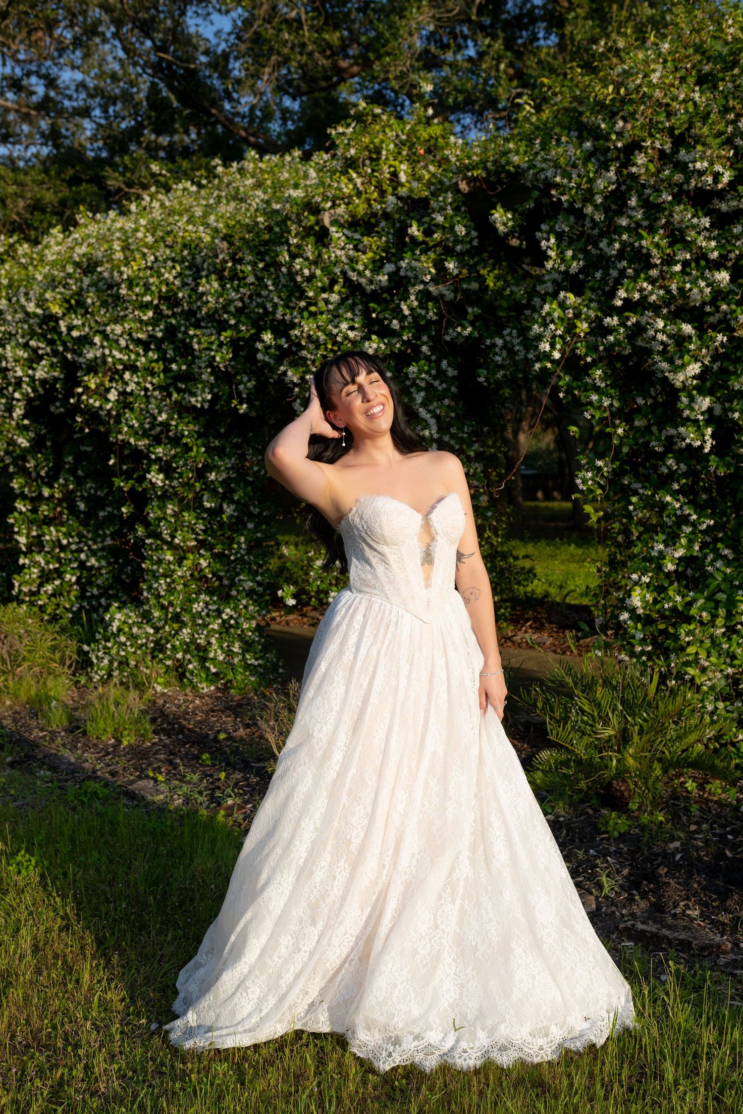 Bride in strapless lace ball gown poses beneath a floral arch in golden evening light.