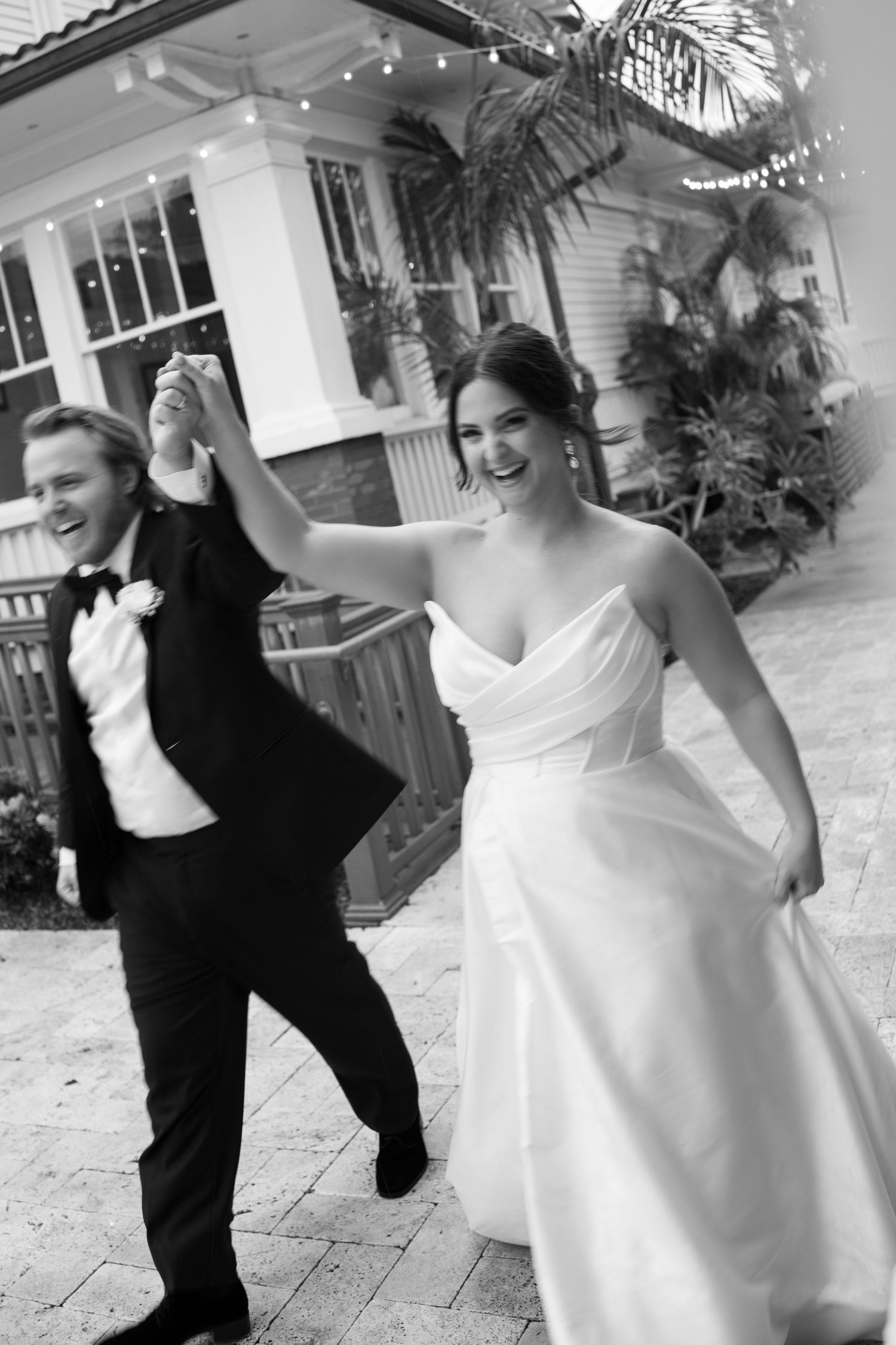 Bride and groom dancing joyfully outside wedding venue in black and white.