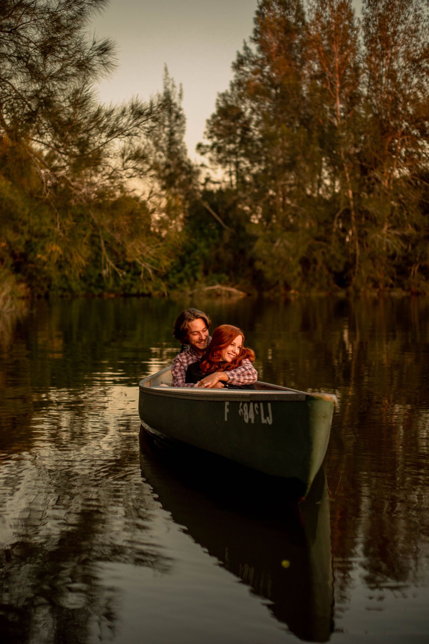 Couple cuddling together in a canoe on a serene lake with colorful fall trees reflected in water.