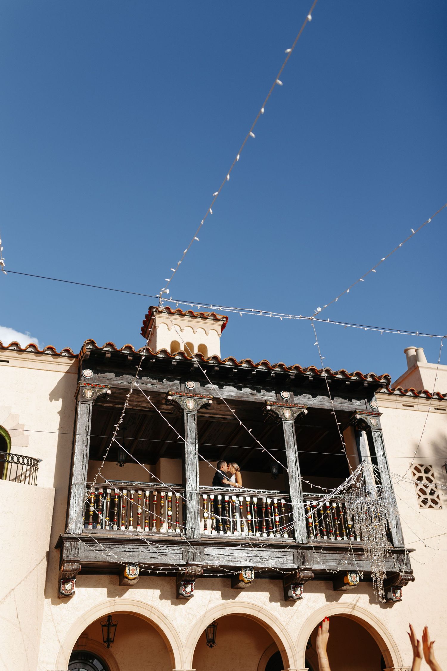 Spanish-style wedding venue balcony decorated with sparkling string lights against a clear blue sky.