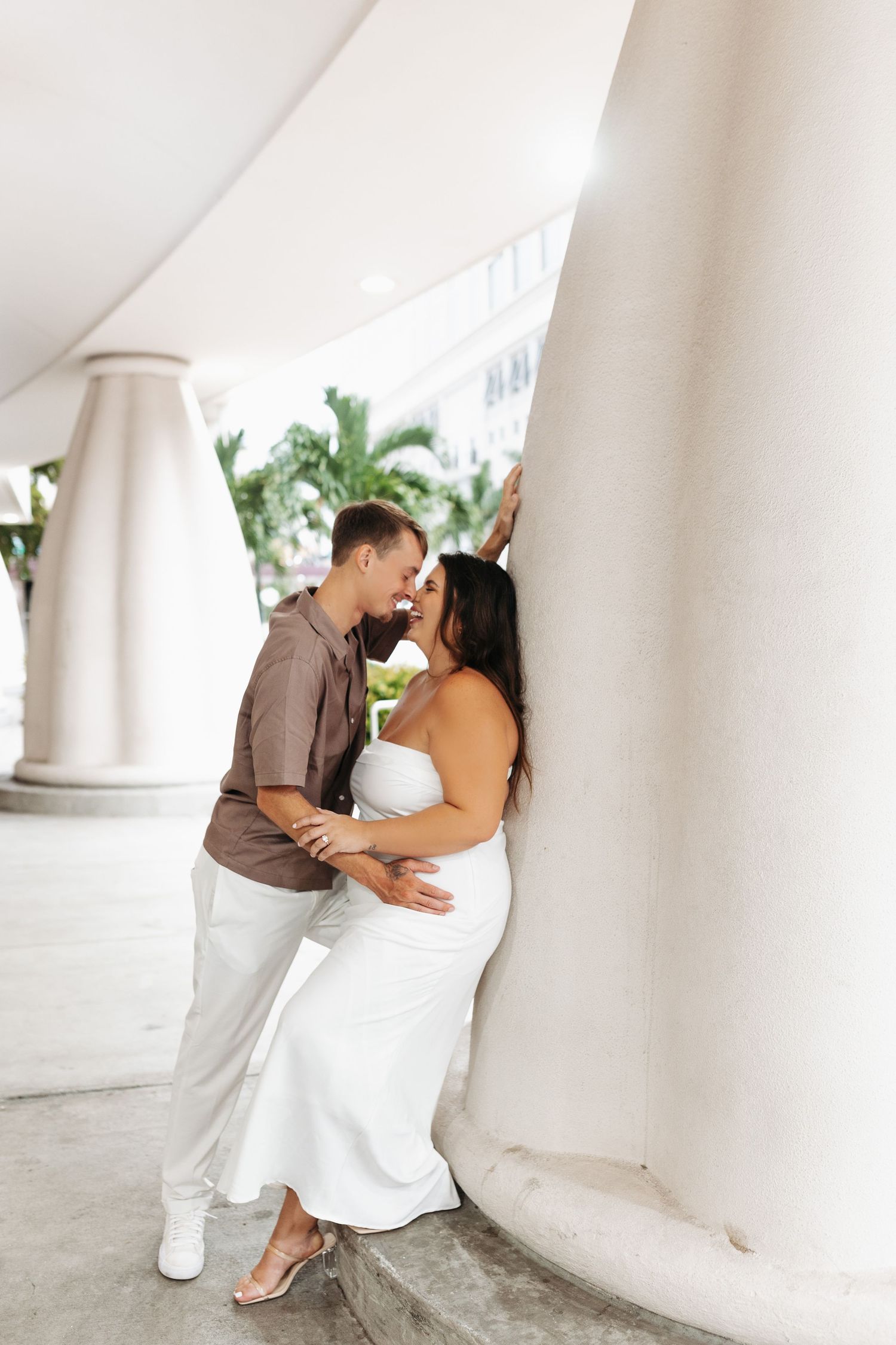 Couple sharing a romantic moment leaning against a white column outdoors.