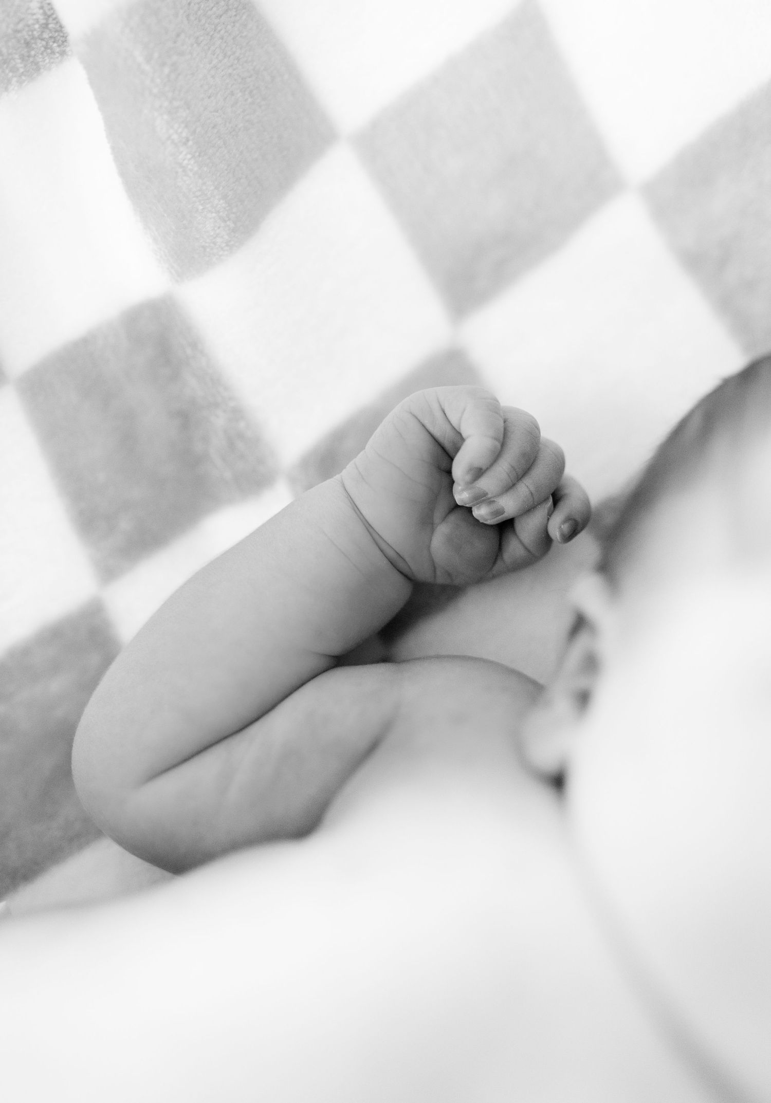 Close-up black and white photo of a newborn babys tiny hands and feet on a soft blanket.