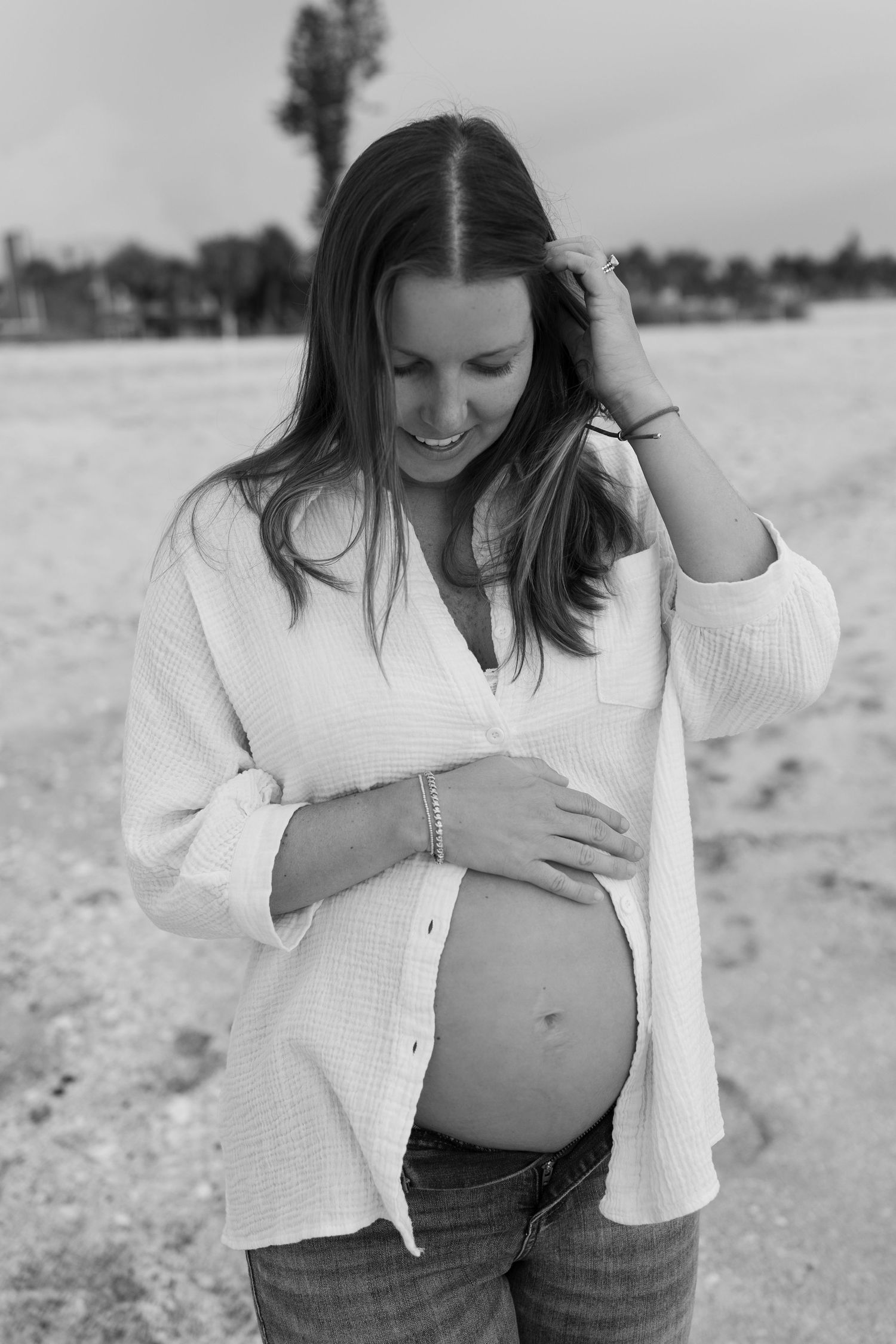 Black and white portrait of a smiling pregnant woman in white shirt cradling her baby bump.