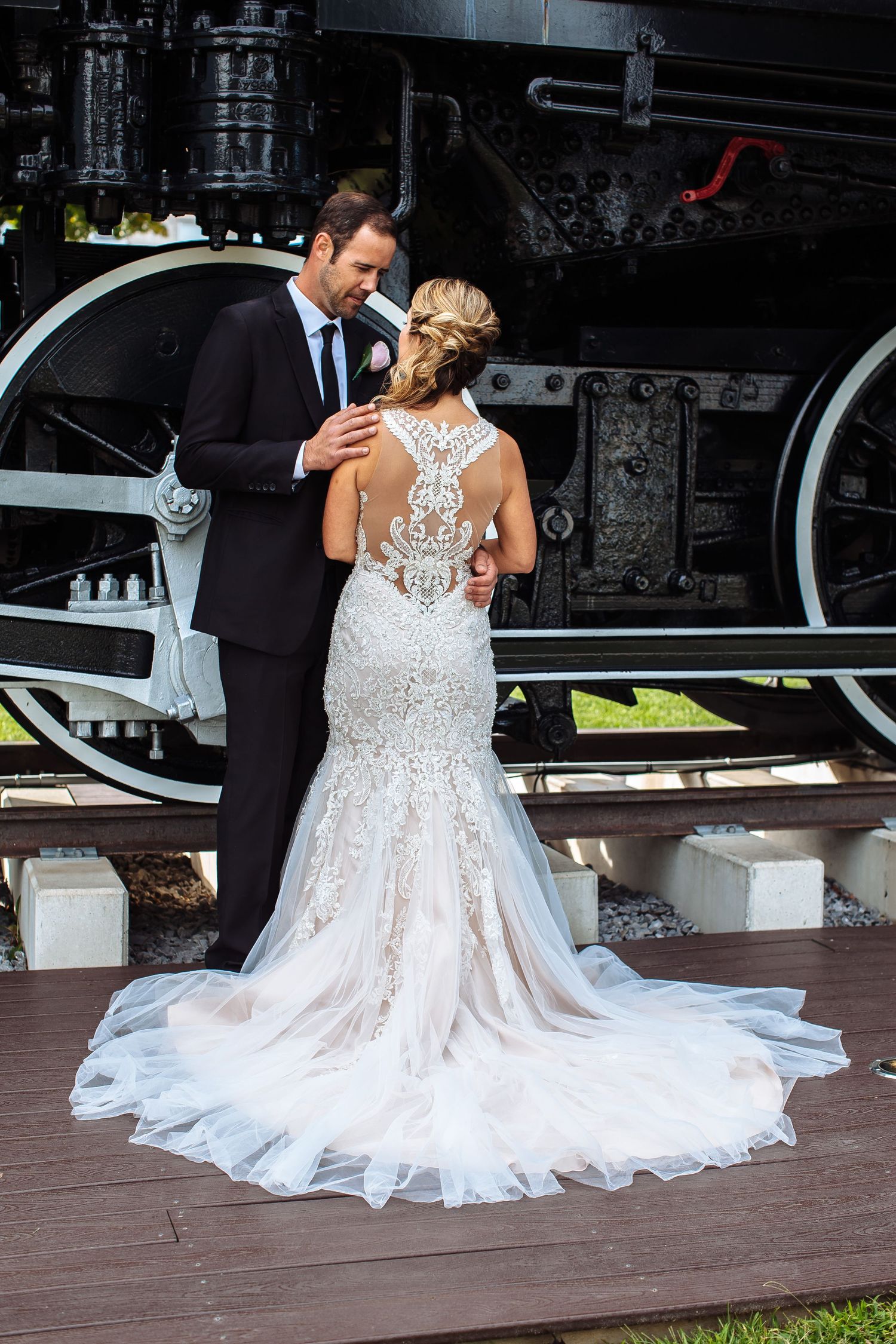 Wedding couple posing by vintage steam locomotive showing detailed lace back dress.