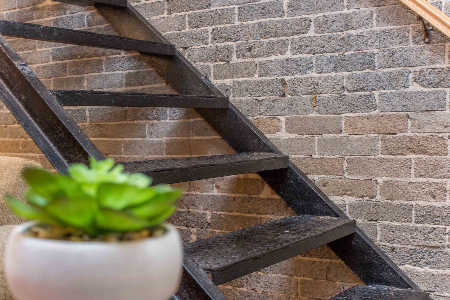 Modern staircase with black metal railings against exposed brick wall and decorative succulent.