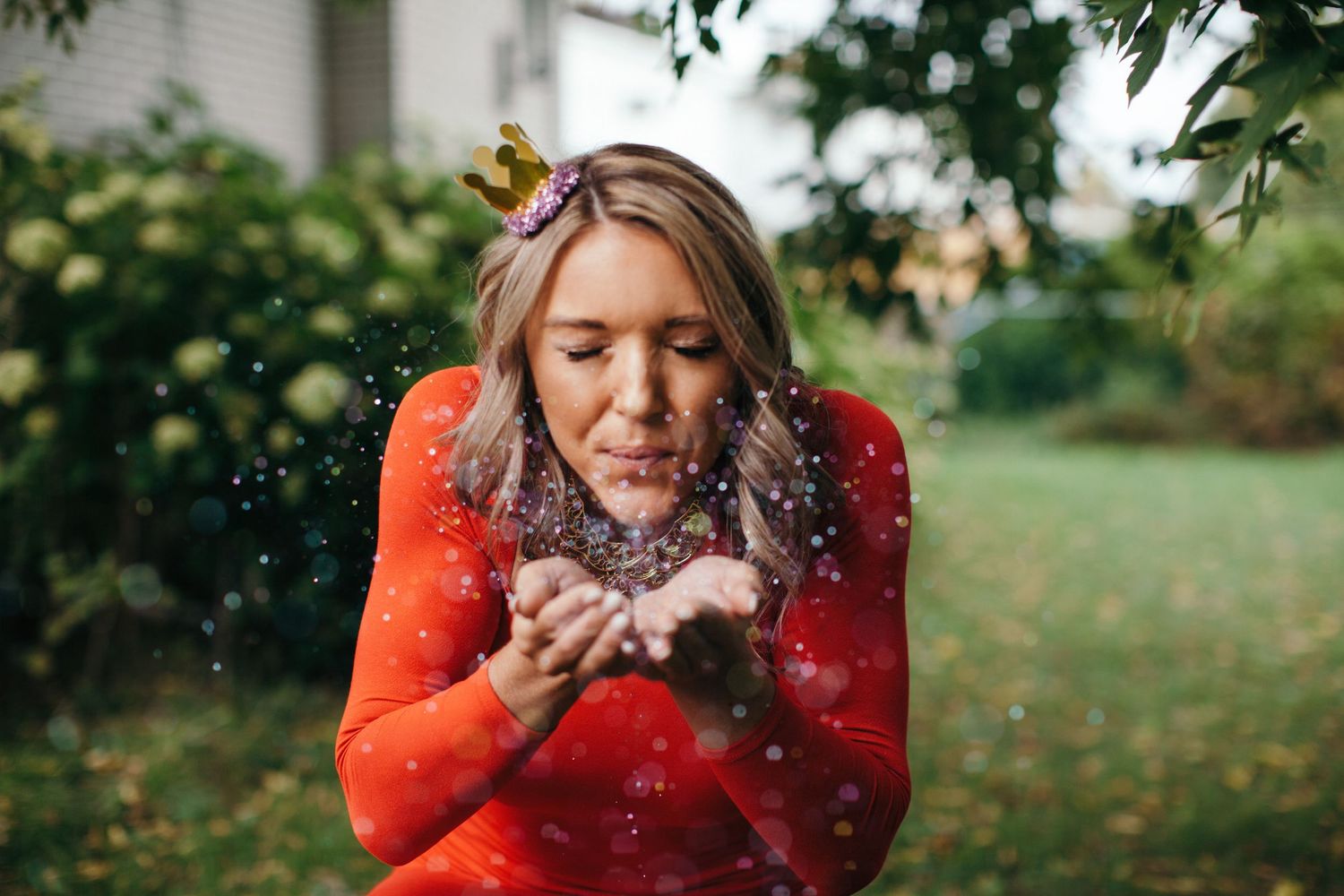 Person in red sweater blowing glitter in outdoor autumn setting.