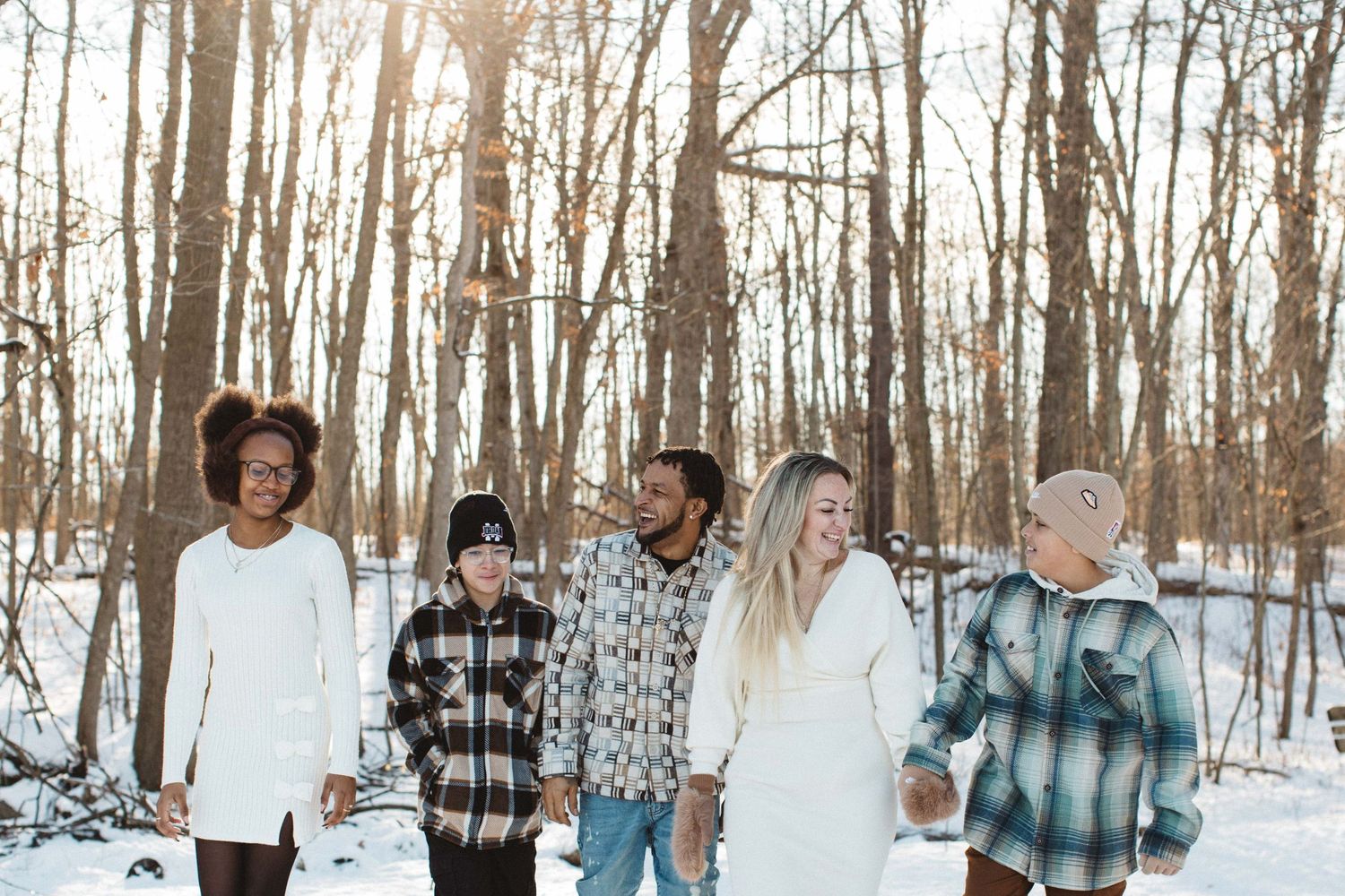 Family walking together through snowy winter forest during lifestyle photo session.