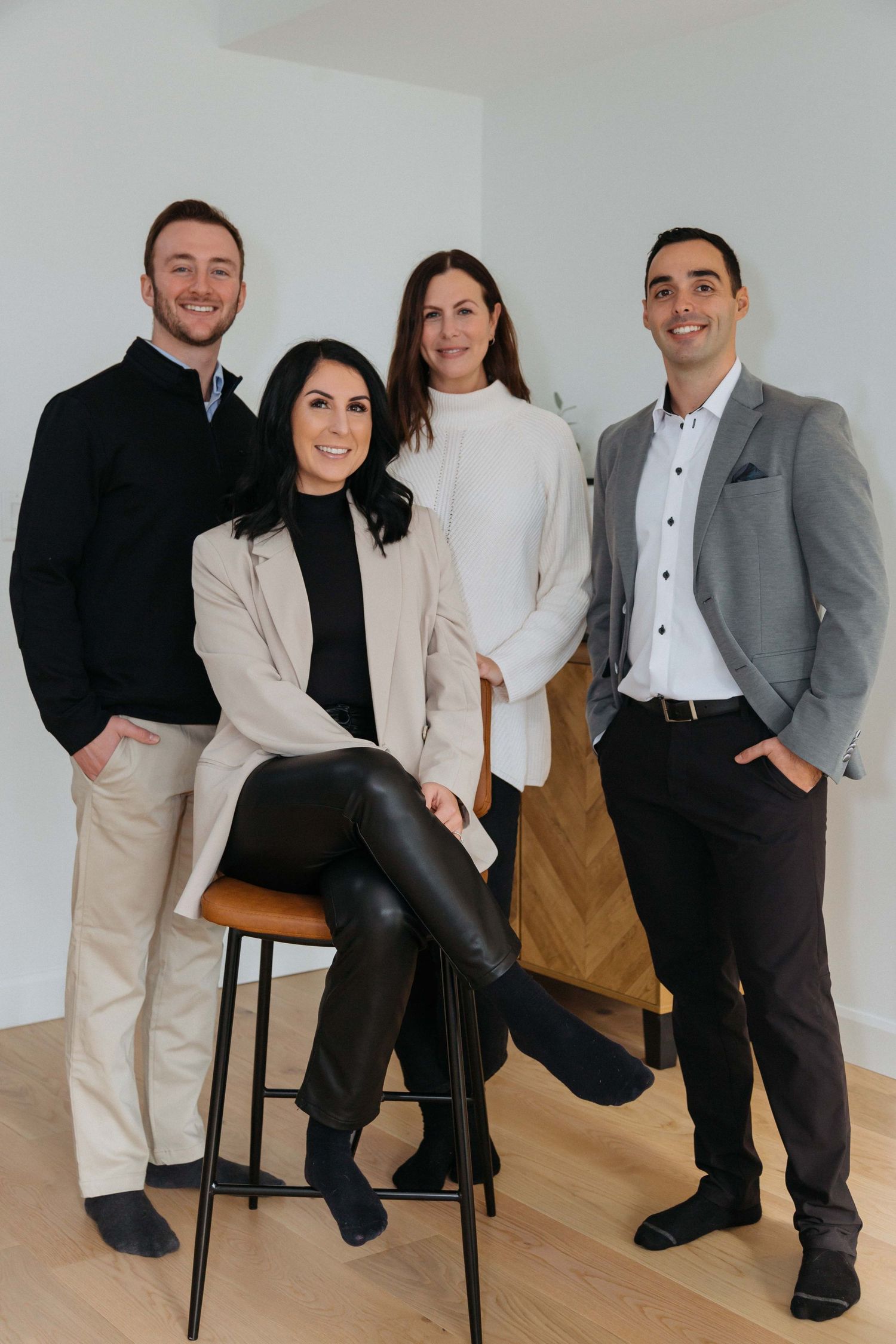 Professional team in formal attire posing together on chairs in modern studio setting.