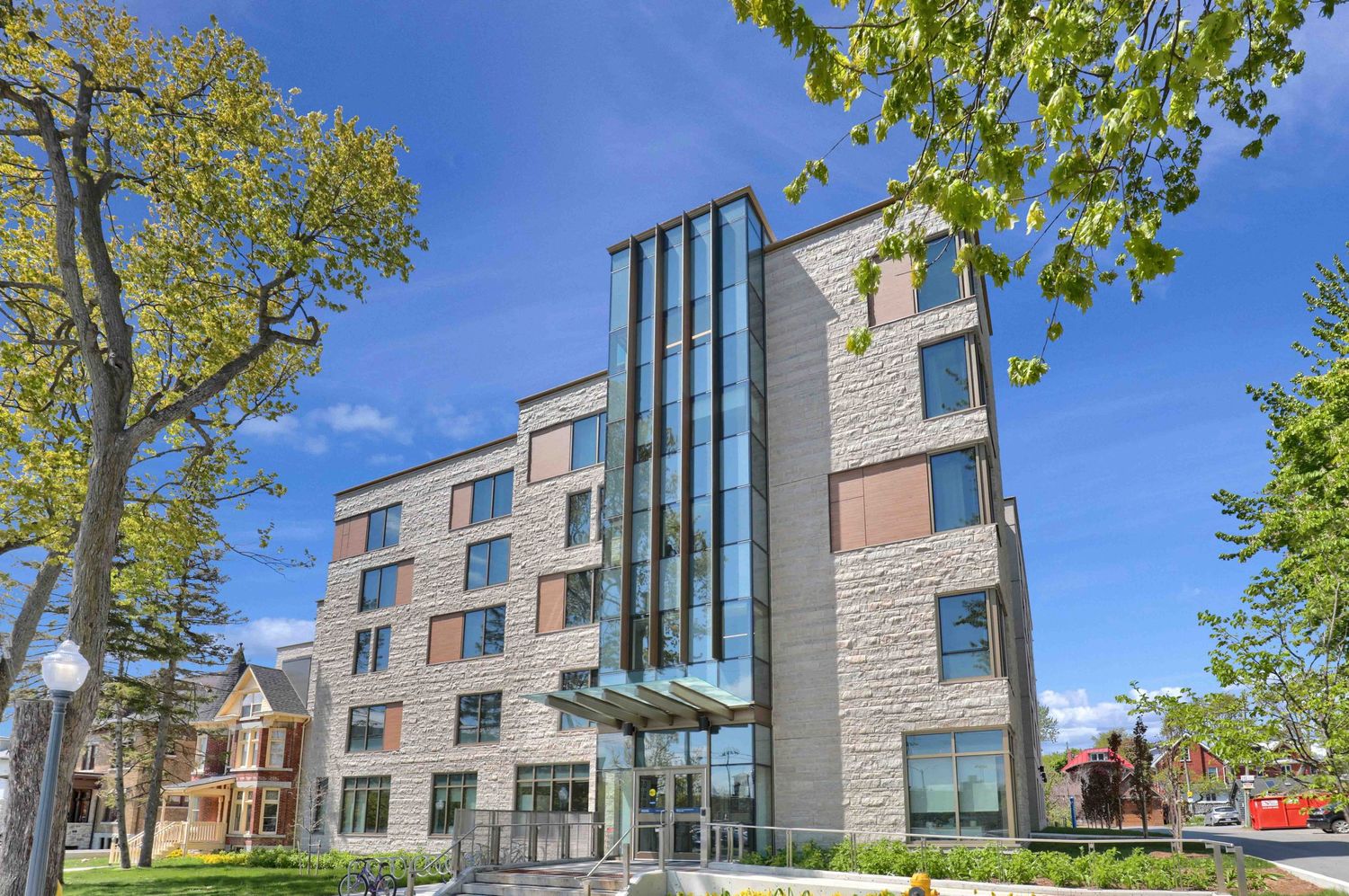 Modern stone and glass apartment building exterior with trees and blue sky on a sunny day.