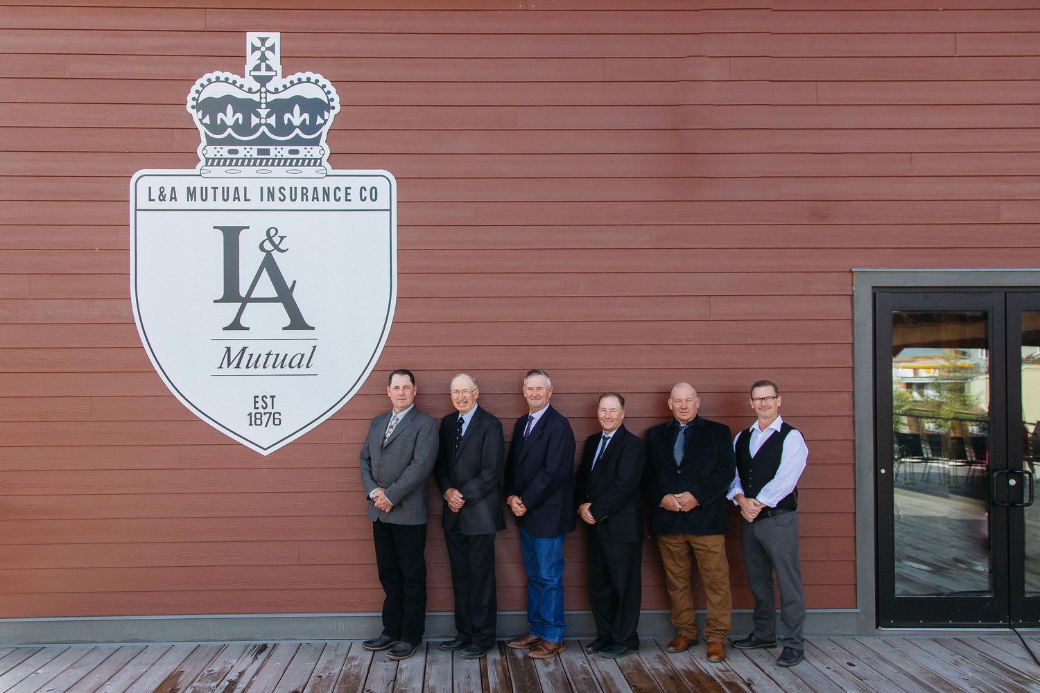Professional group photo taken outside a brick building with vintage-style signage.