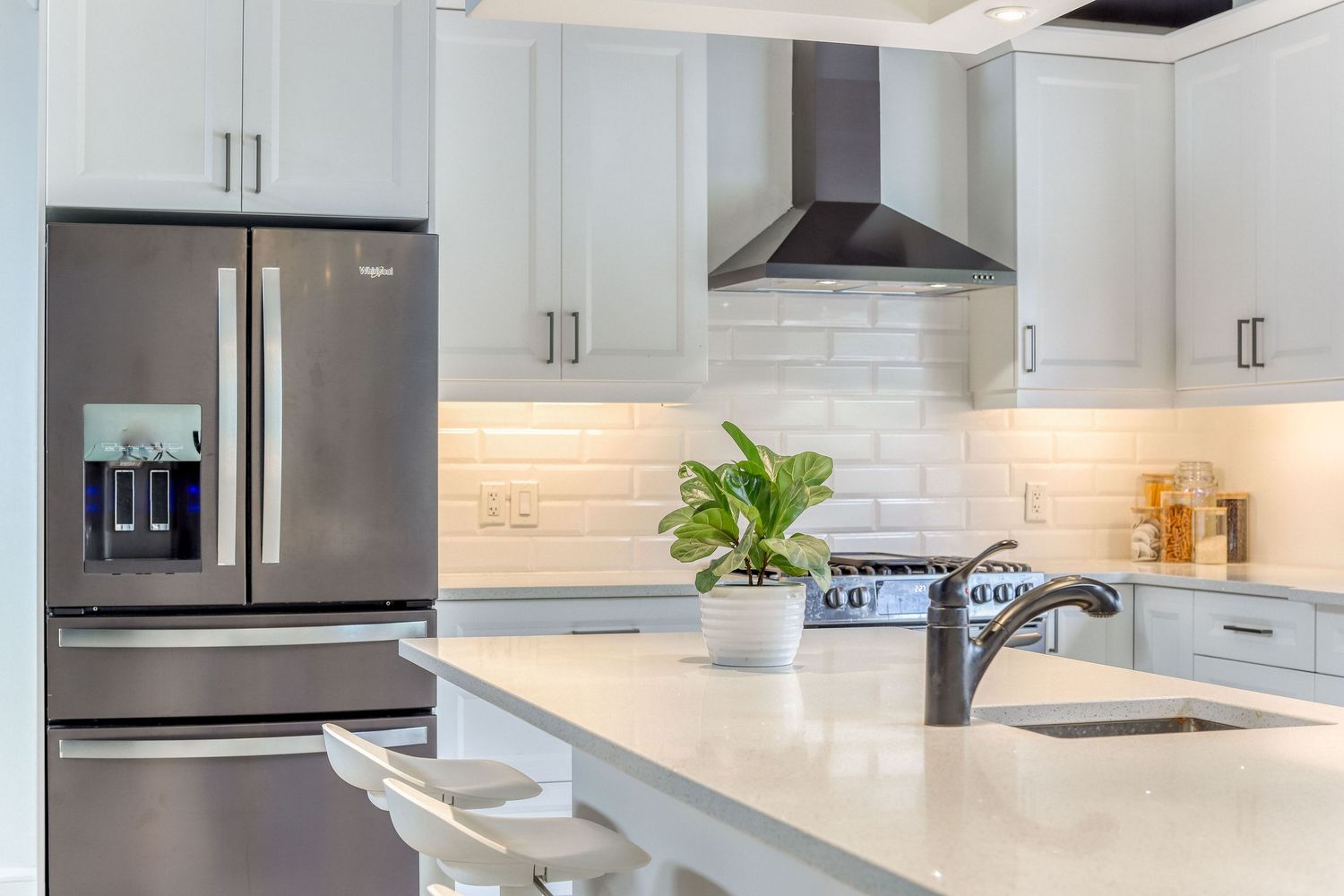 Bright modern kitchen featuring white cabinets, stainless appliances, and marble countertops.