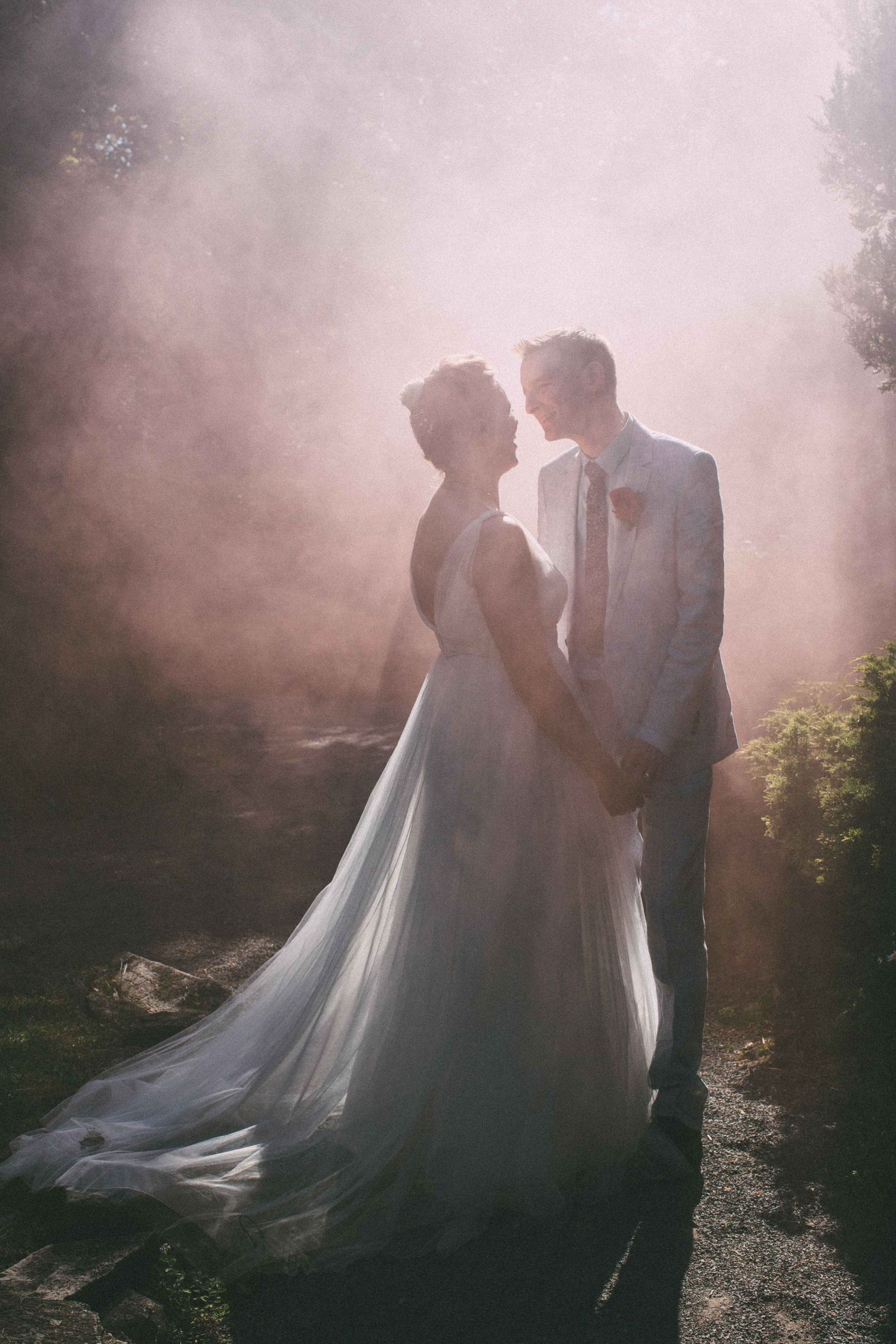 An ethereal wedding portrait with soft pink smoke effects creating a dreamy atmosphere.