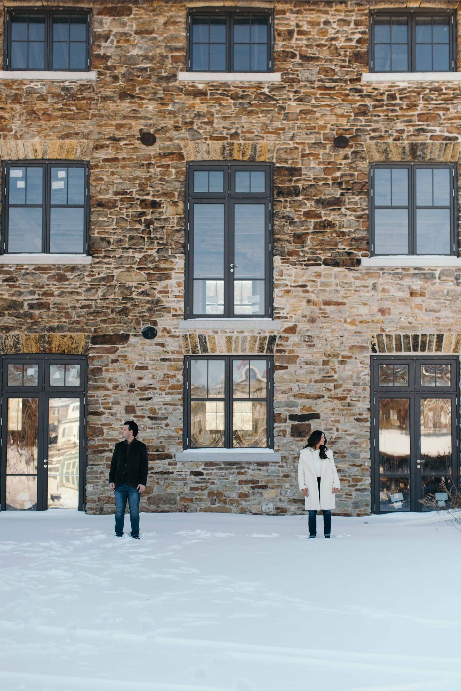 People standing against historic brick building facade with large windows in snow.