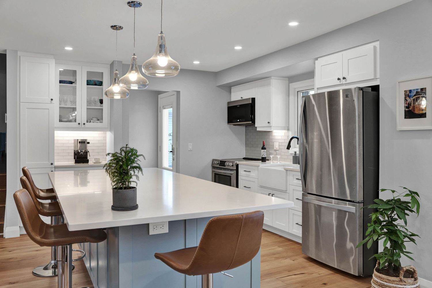 Contemporary white kitchen with stainless steel appliances, pendant lights, and brown bar stools.