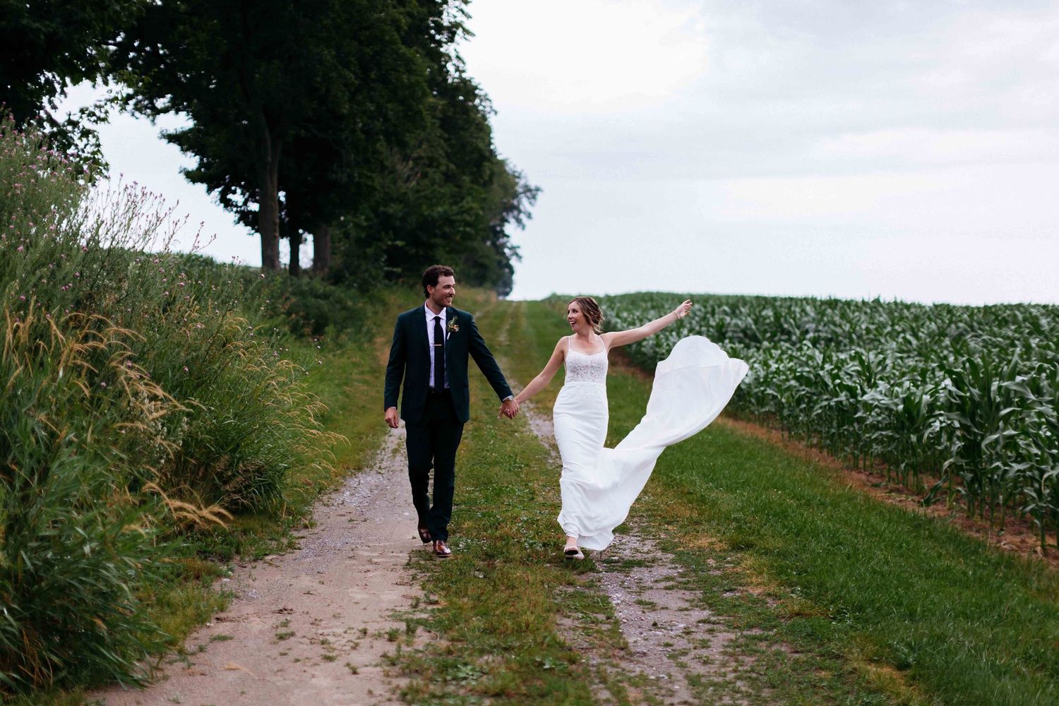 Romantic countryside wedding photo with flowing dress on dirt path between crops.