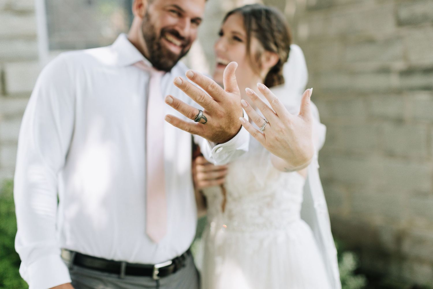 Newlywed couple showing off their wedding rings with joyful expressions in outdoor setting.