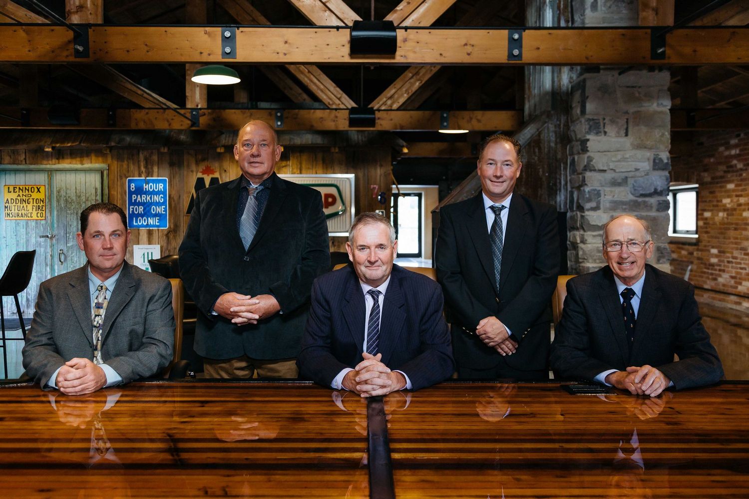 Business executives seated along a wooden bar in a rustic meeting space.