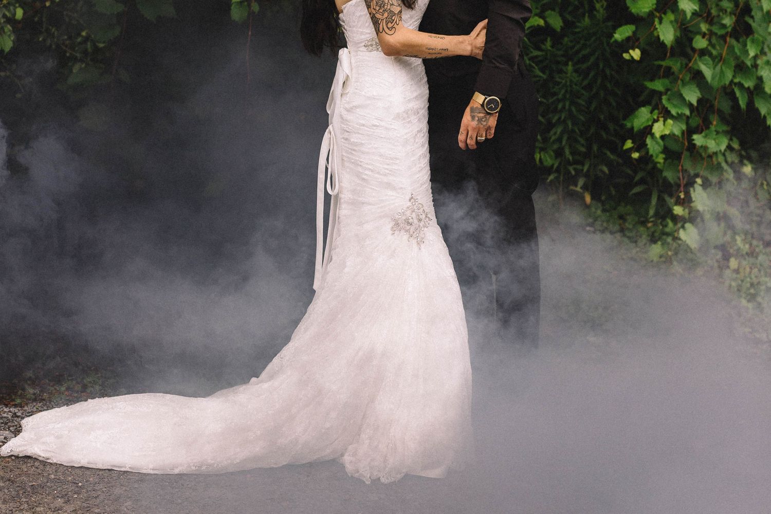 Bride in flowing white dress surrounded by dramatic fog effects outdoors.