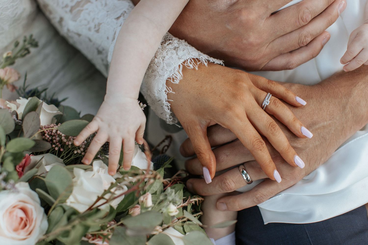 Close-up of wedding rings and hands with pink roses and greenery.