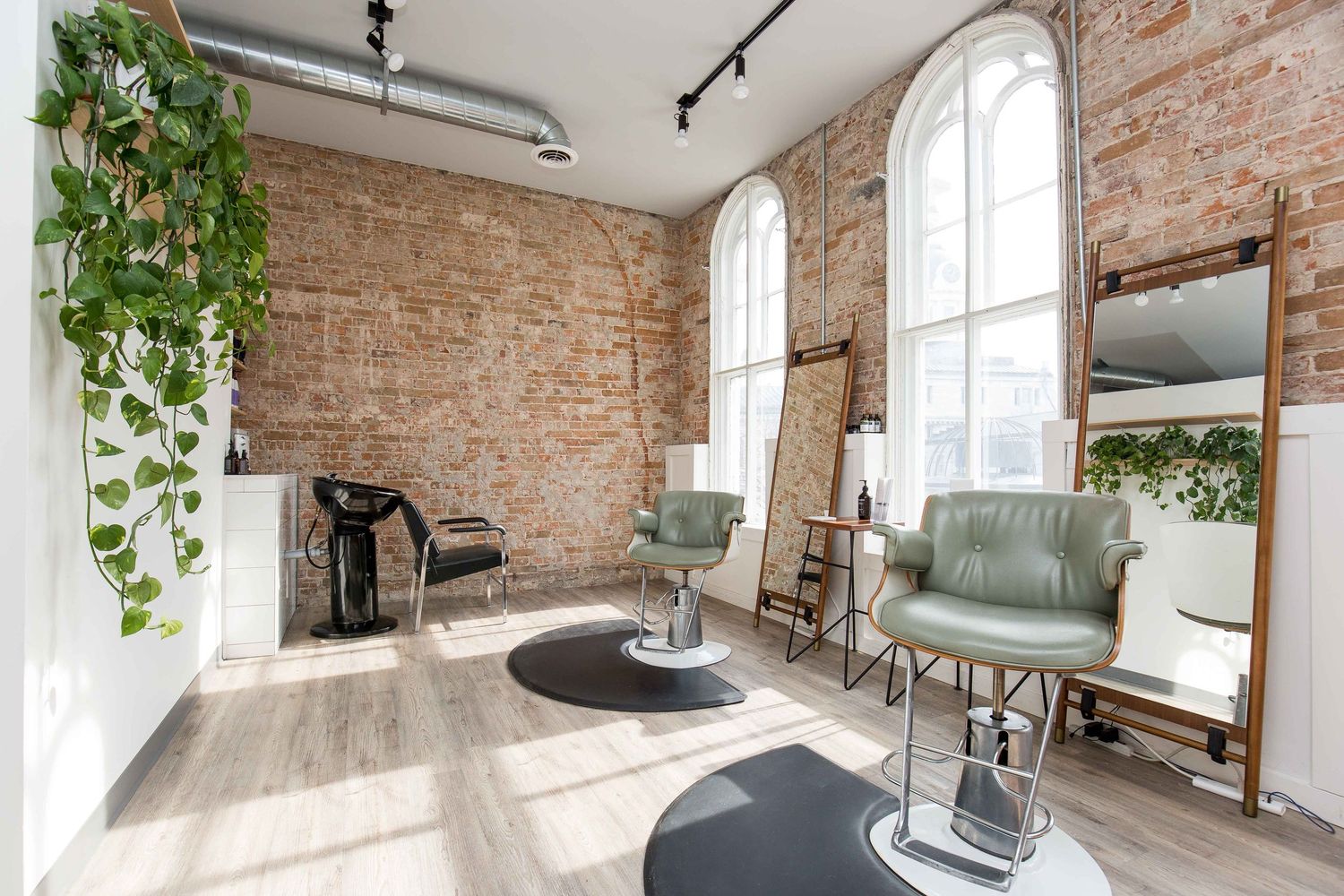 Industrial-chic living room featuring exposed brick walls, tall windows, and hanging plants.