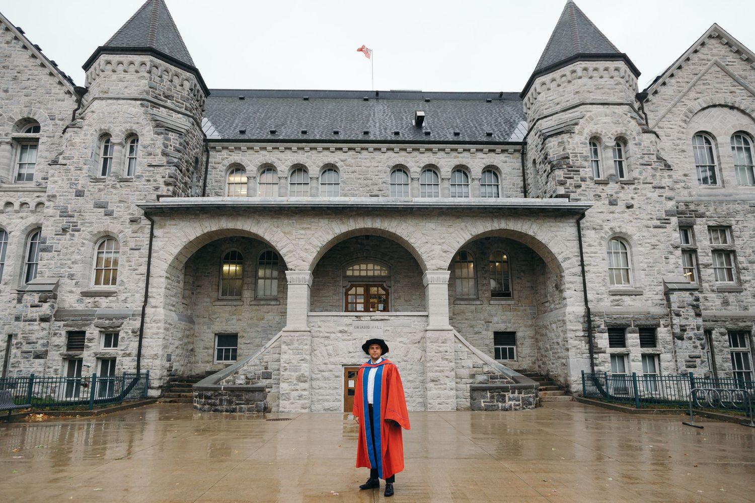 Graduate in academic regalia standing in front of historic stone castle-like university building.
