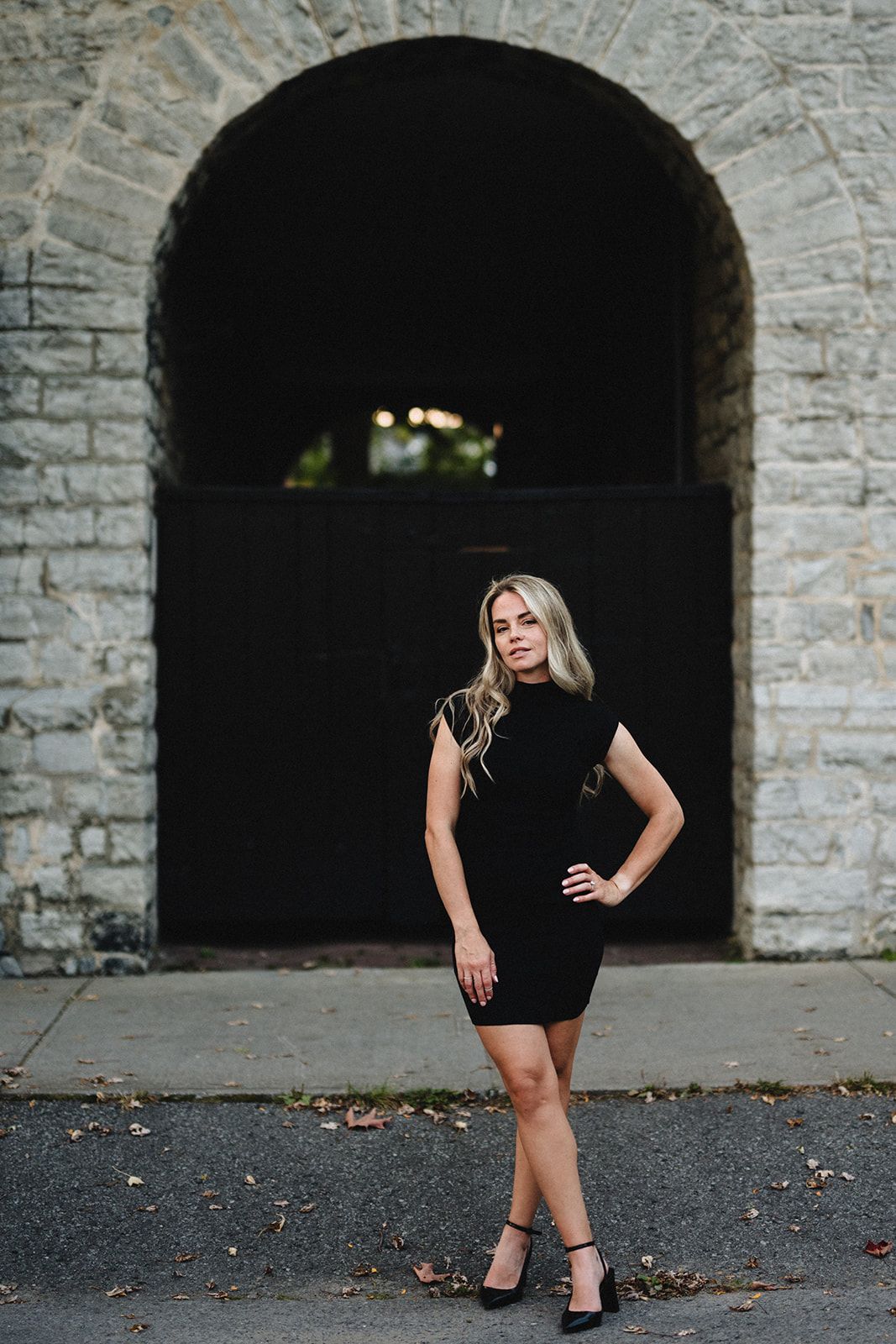 A stylish portrait under a stone archway featuring a black cocktail dress and heels.