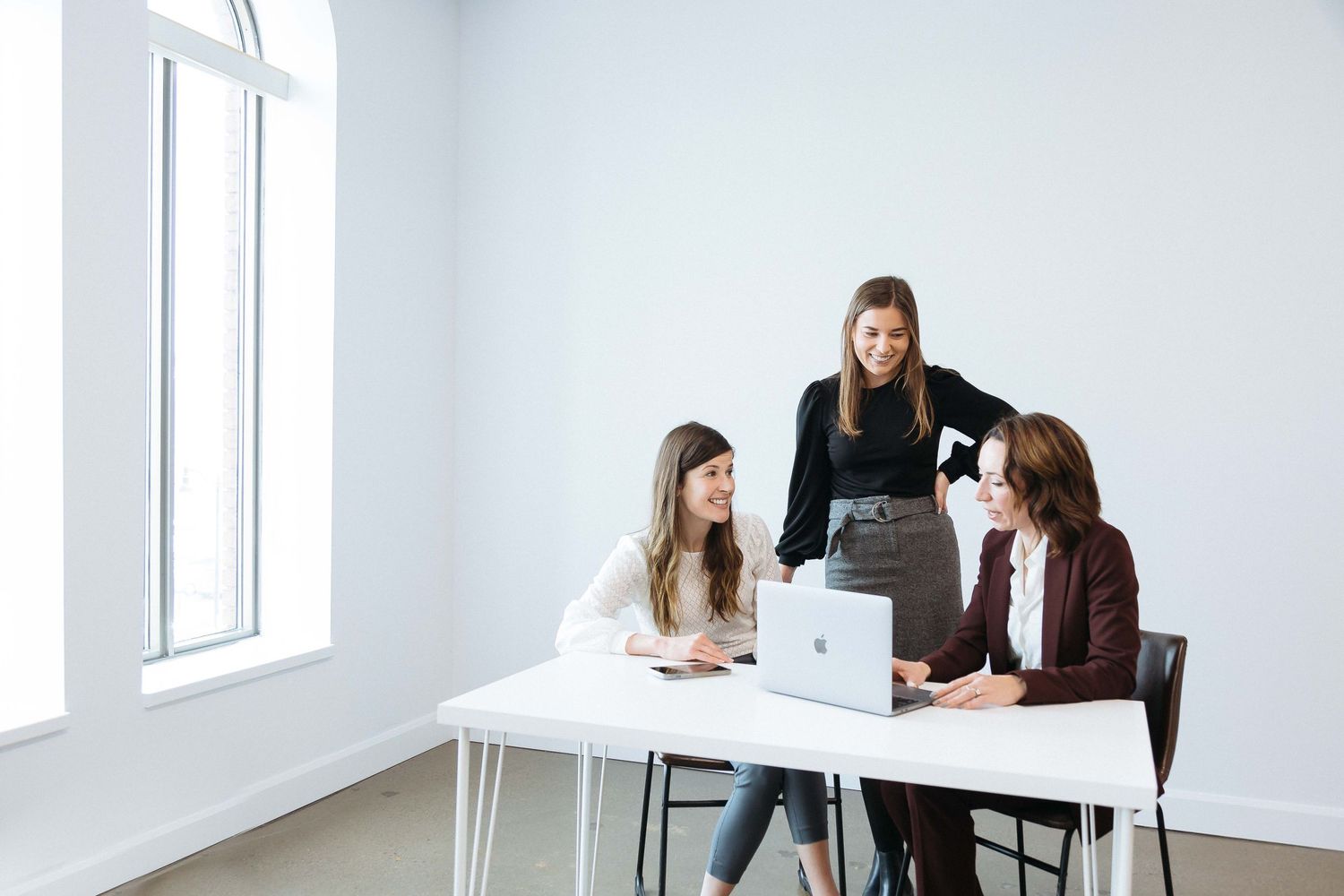 Professional working at modern white desk with laptop in bright minimalist office space.
