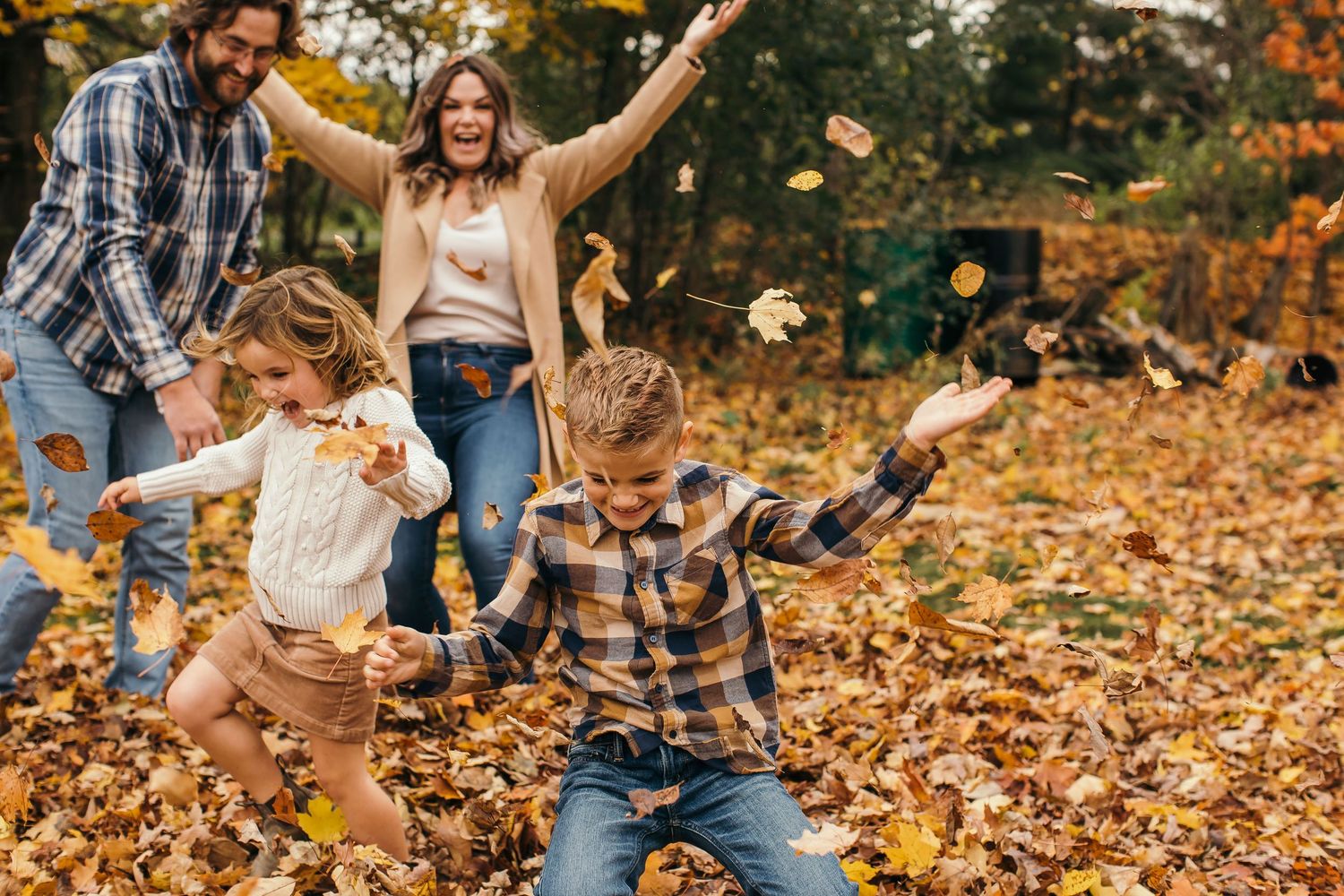 Family playing and throwing autumn leaves in the air during golden hour at a park.