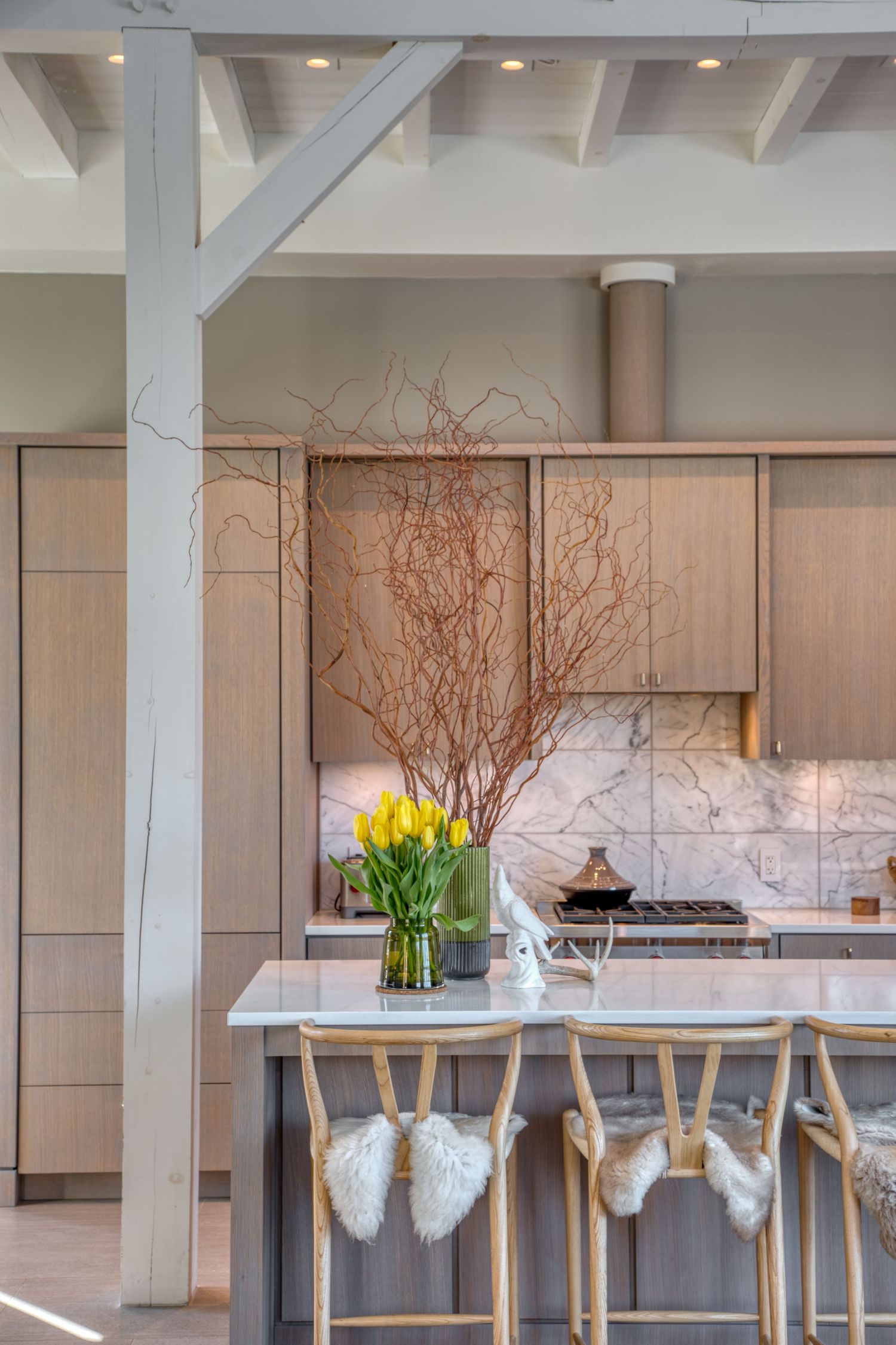 Modern kitchen interior with yellow tulips and branch decor on marble countertop.