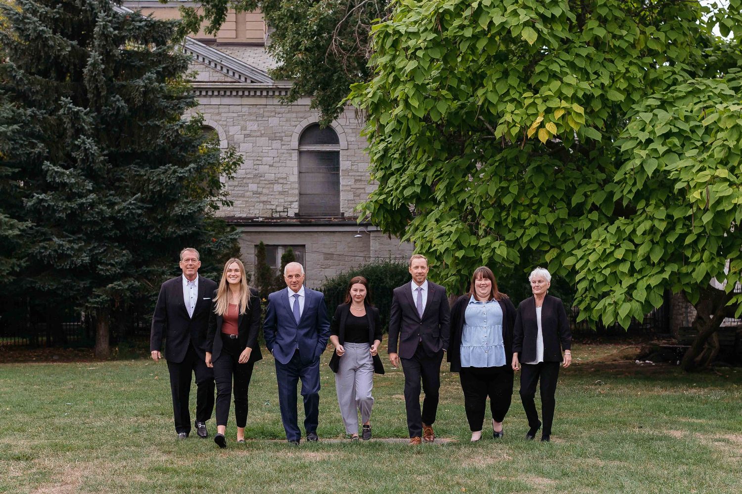 Professional group photo of business team standing together outdoors in front of stone building.