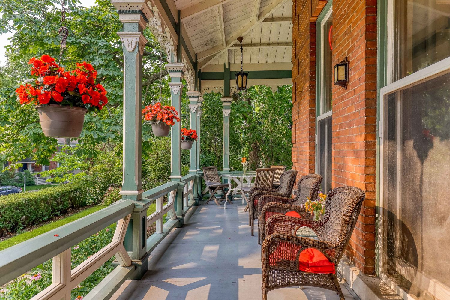 Wrap-around porch with rocking chairs and red floral hanging baskets.