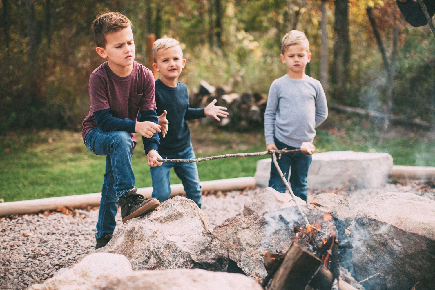 Children playing around a smoky campfire in an outdoor setting.