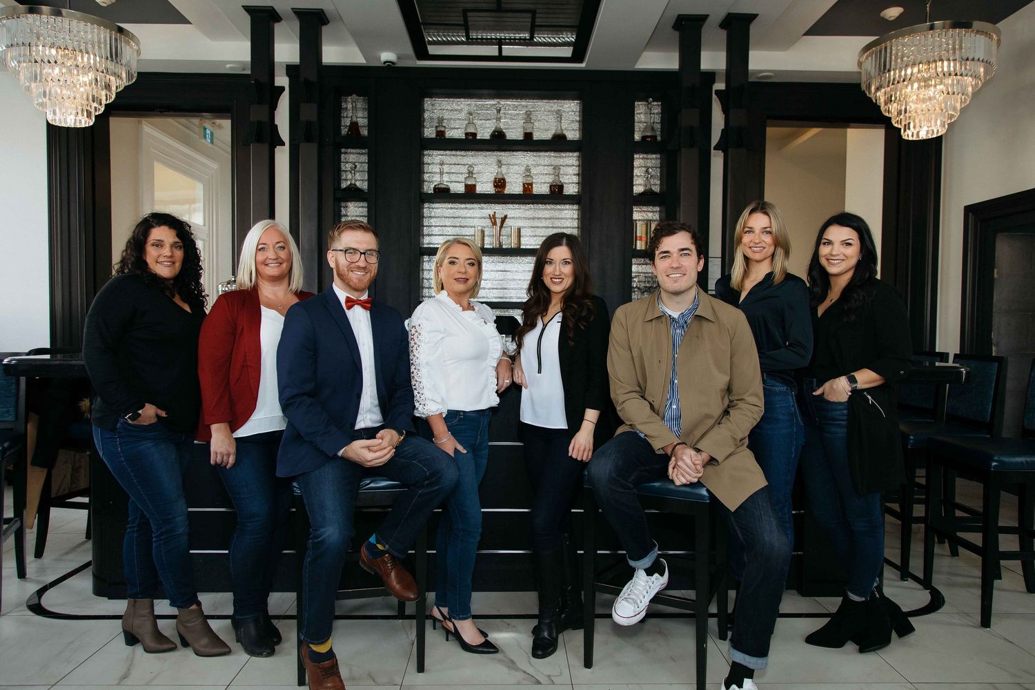 Group photo of business team members in modern office space with chandelier lighting.