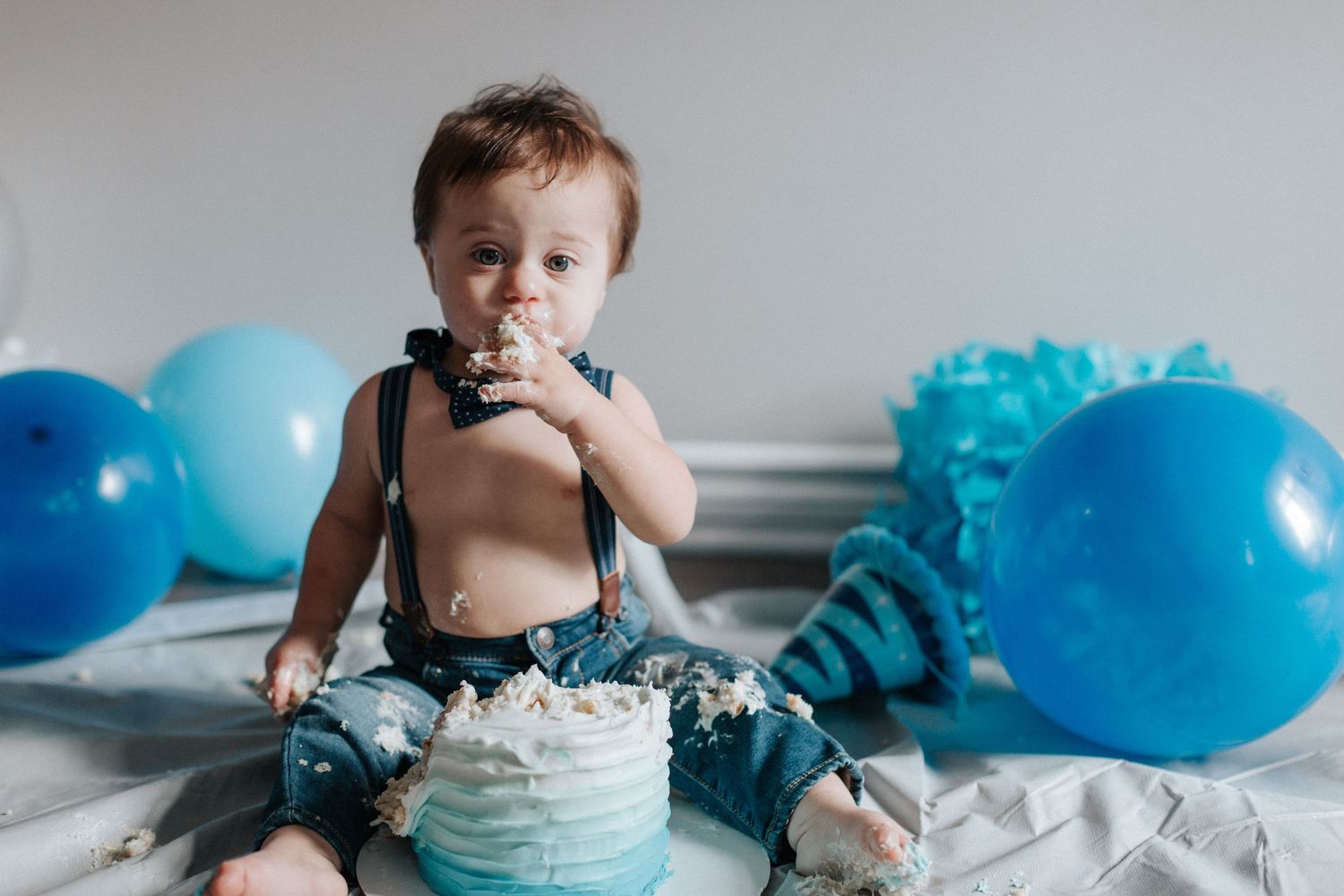 Baby celebrating with blue balloons and cake during first birthday smash cake photo session.
