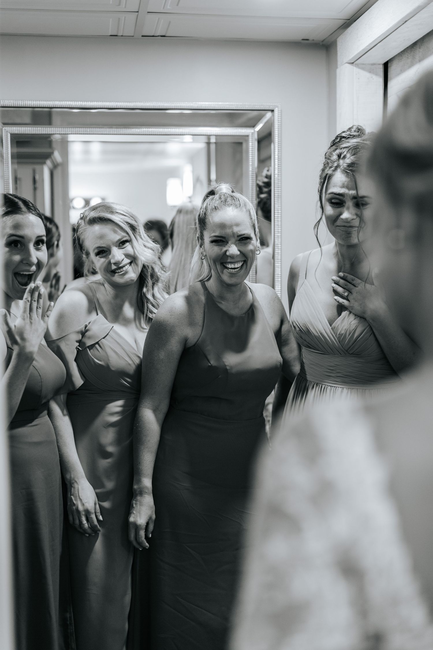 Candid black and white photo of bridesmaids sharing joyful moment in hallway.