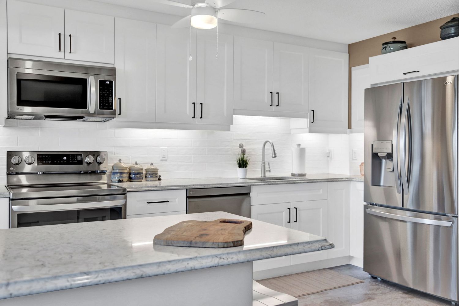 White modern kitchen with stainless steel appliances and extended marble countertop island.