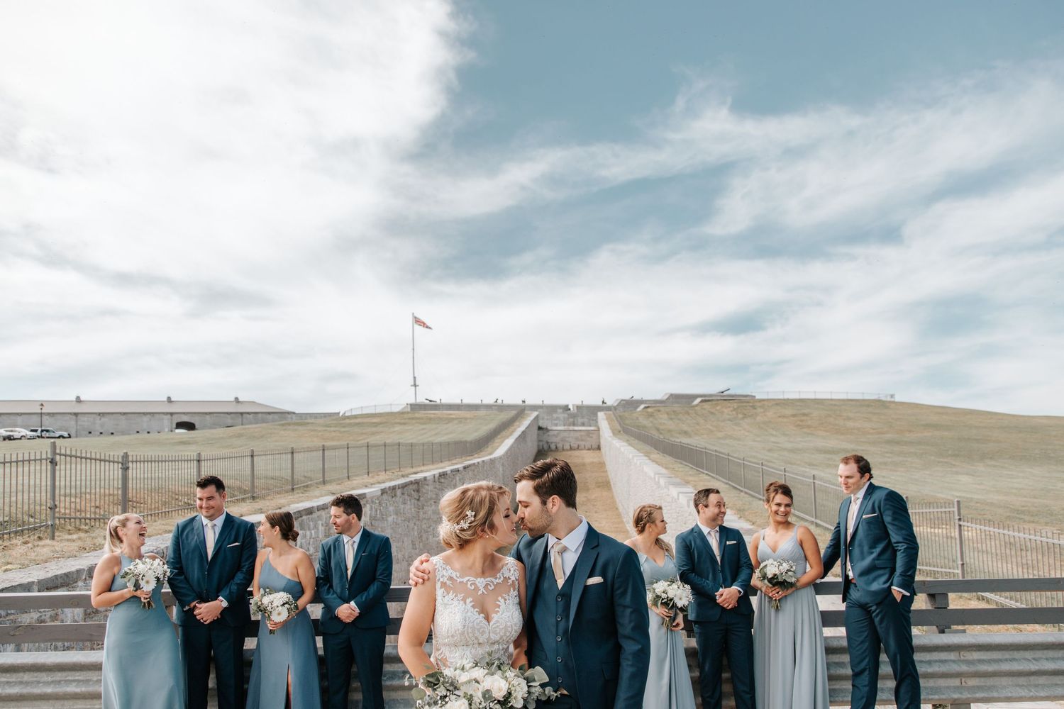 Wedding party lined up against dramatic sky with bridesmaids in blue dresses.