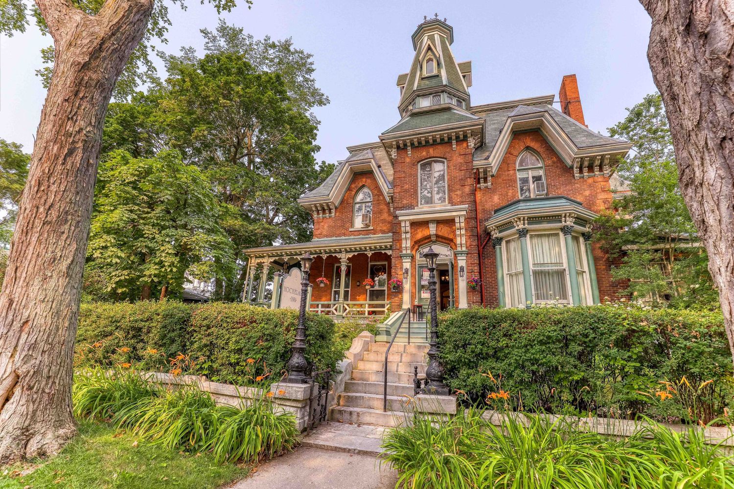 Historic Victorian brick mansion with landscaped garden path and mature trees.