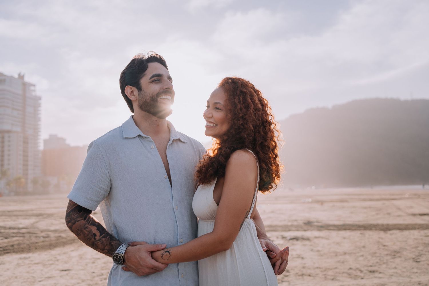 Romantic couple embracing on sandy beach with ocean waves in background.