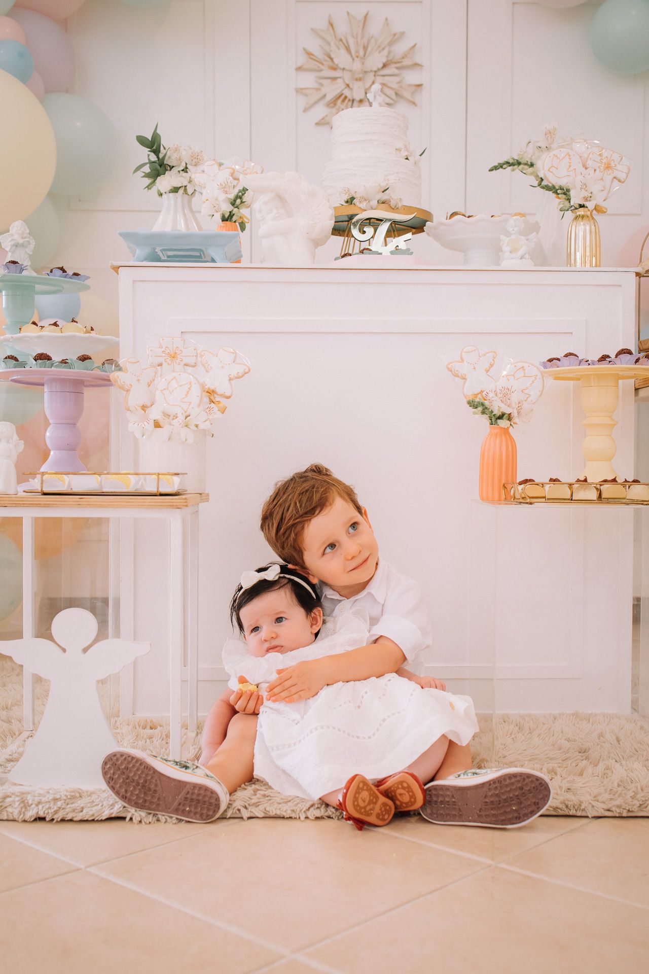 Baby in white outfit lying on floor with pastel decor and shelving in background.