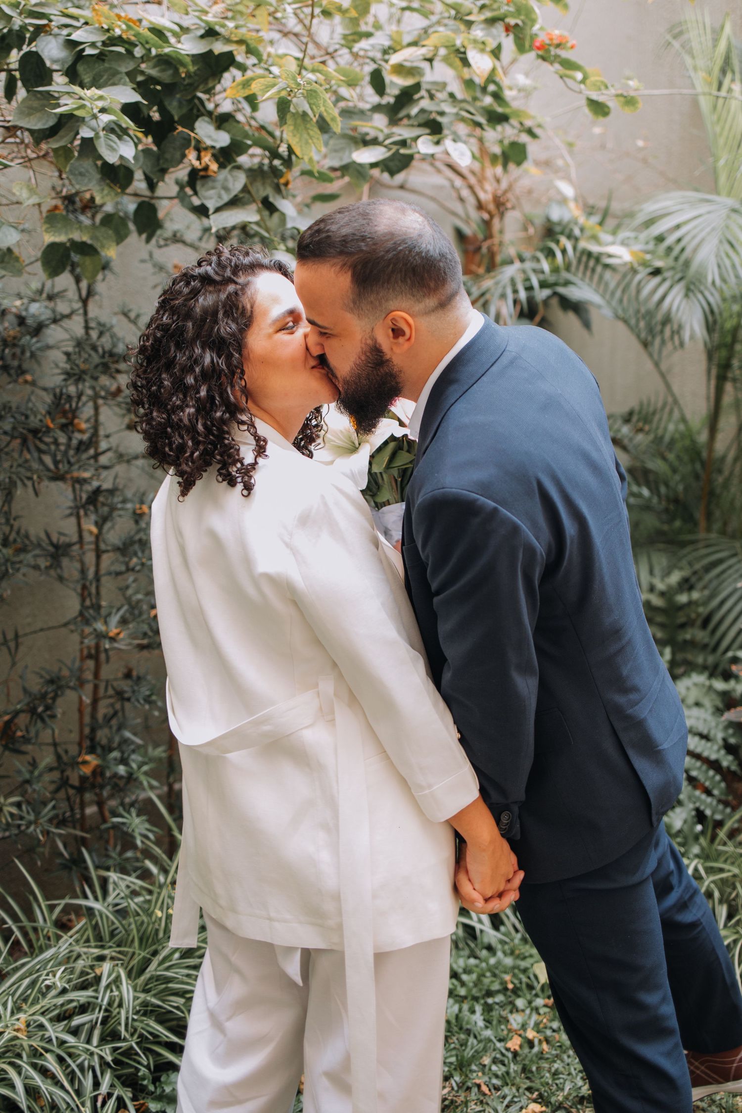 A couple shares an intimate moment in a garden setting wearing contrasting white and navy outfits.