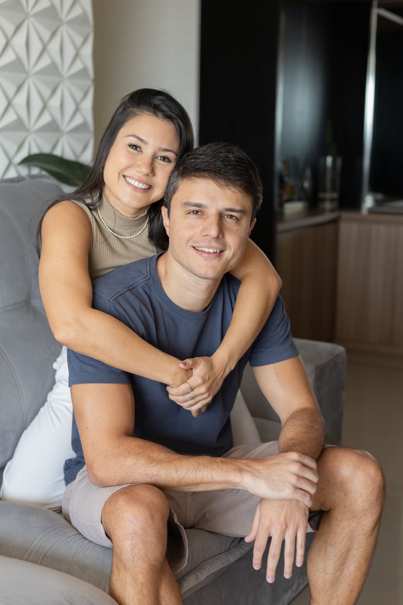 Happy couple embracing on a sofa at home, smiling warmly in a modern living room setting.