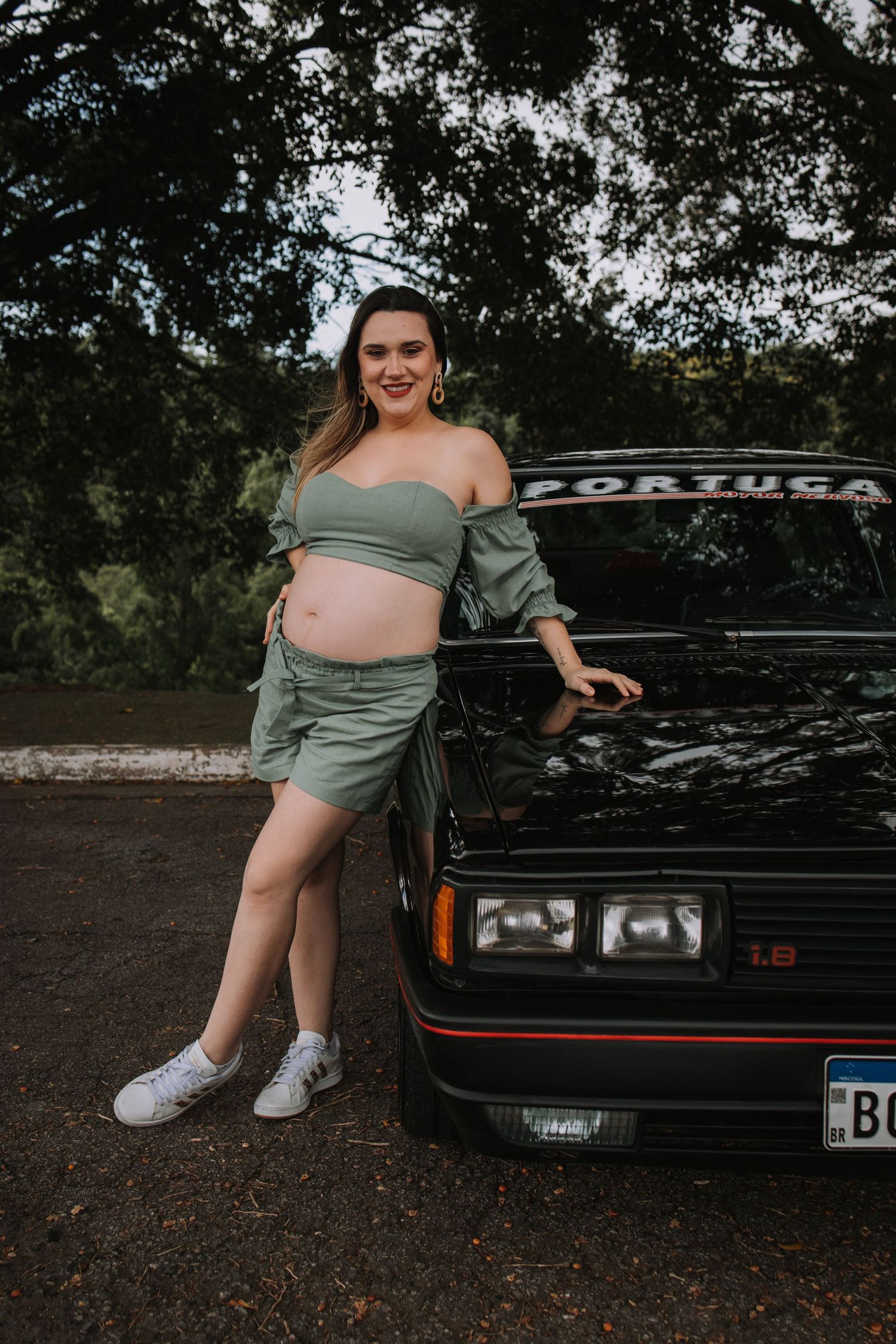 Outdoor maternity shoot featuring classic black car and woman in sage green dress.