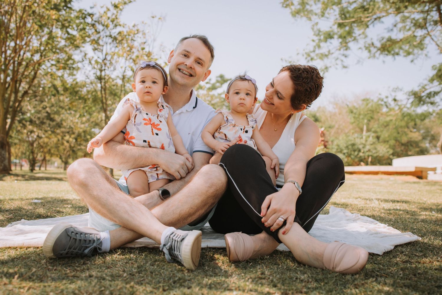 A family enjoys a playful moment together on a blanket in a sunny park setting.