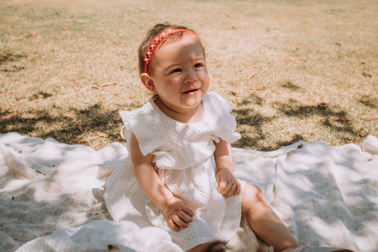 Children laughing while sitting on a white blanket during a sunny outdoor photoshoot.