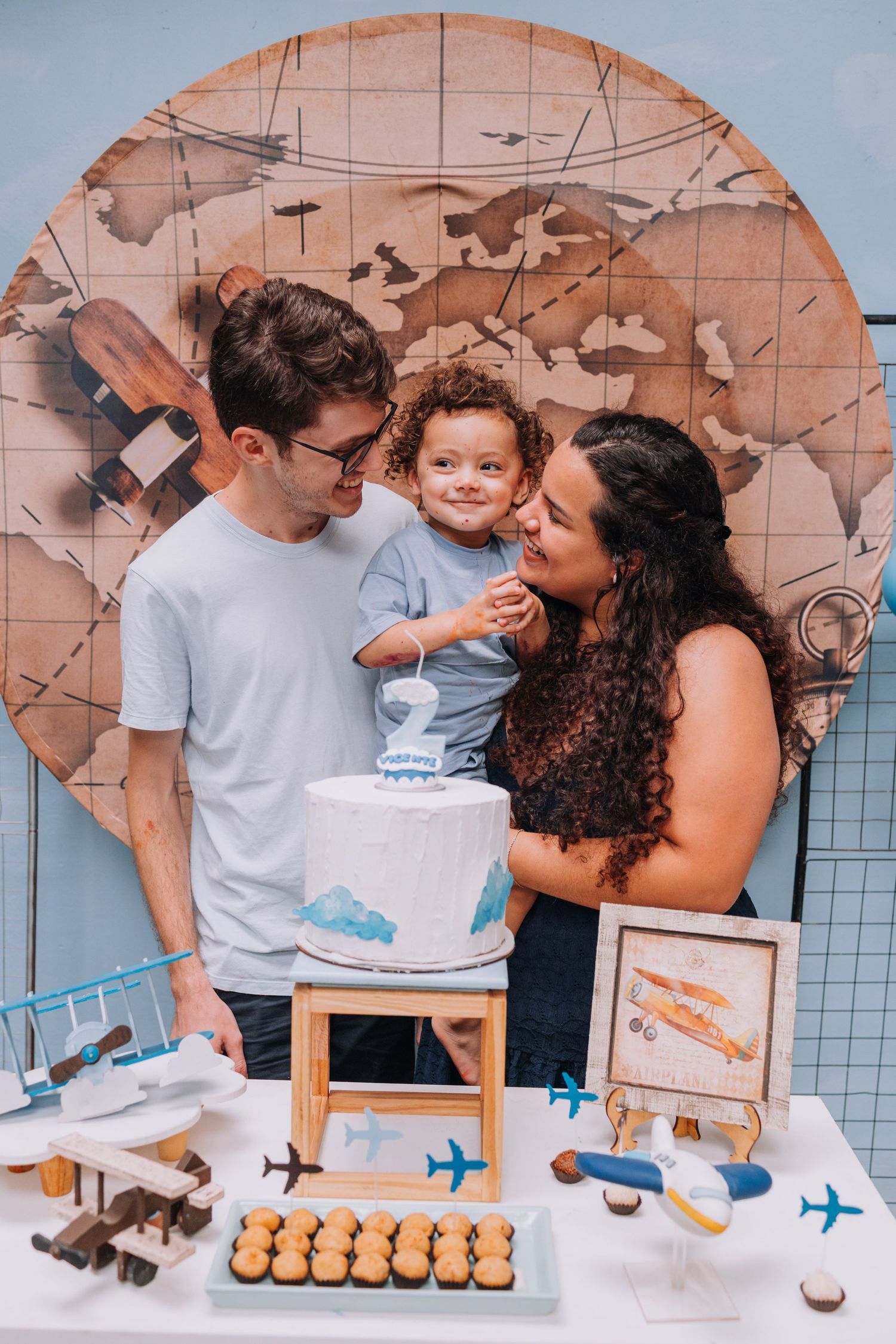Family gathered around a table with a world map backdrop and toy airplanes.
