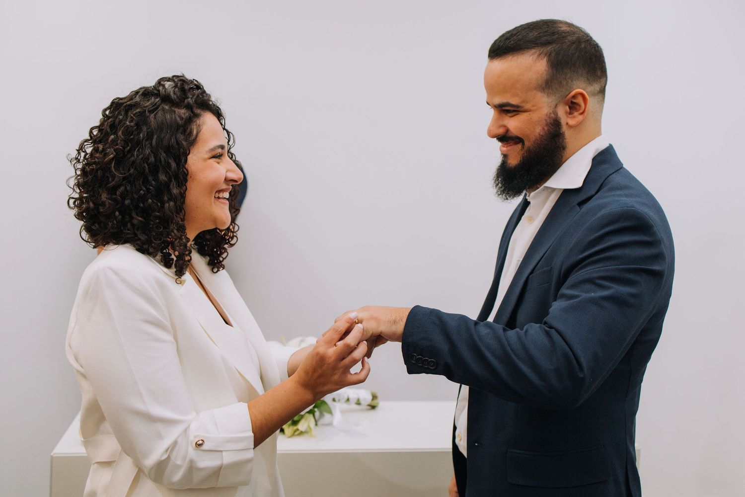 A couple in formal attire shares a tender moment during a wedding photoshoot against a white background.