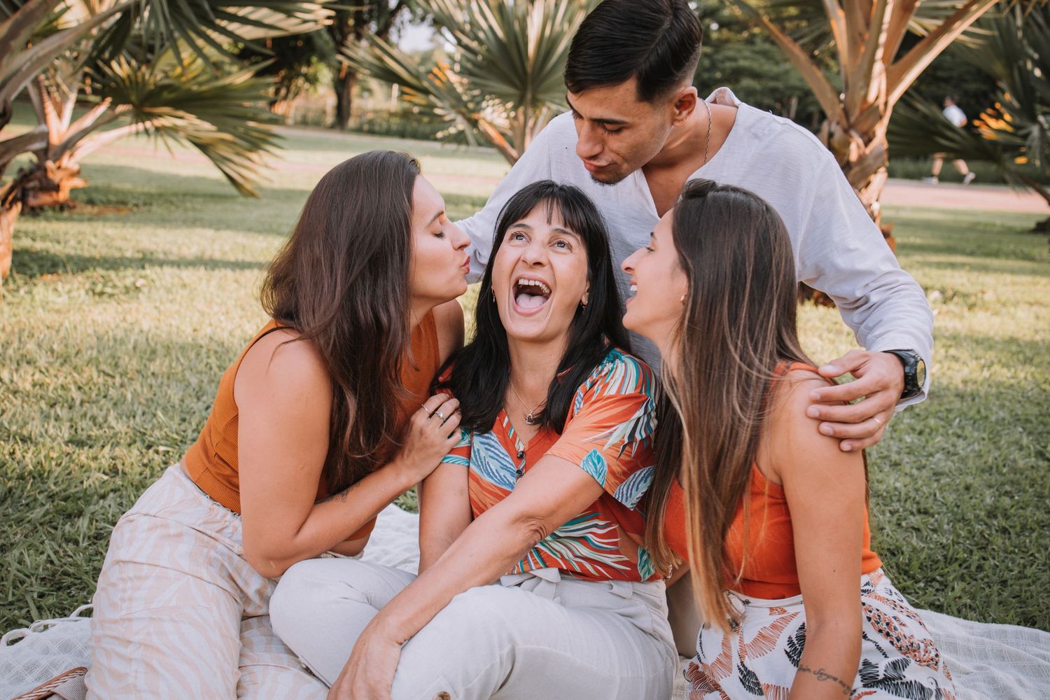 Group sharing joyful laughter while relaxing on blanket during outdoor photo session.