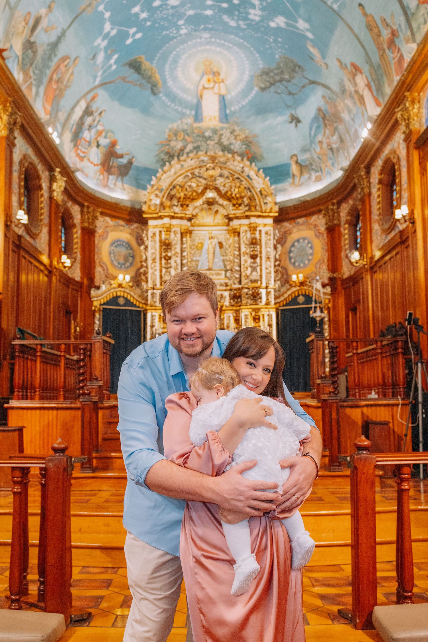 Happy family with baby at ornate church altar with golden decor and painted ceiling dome.