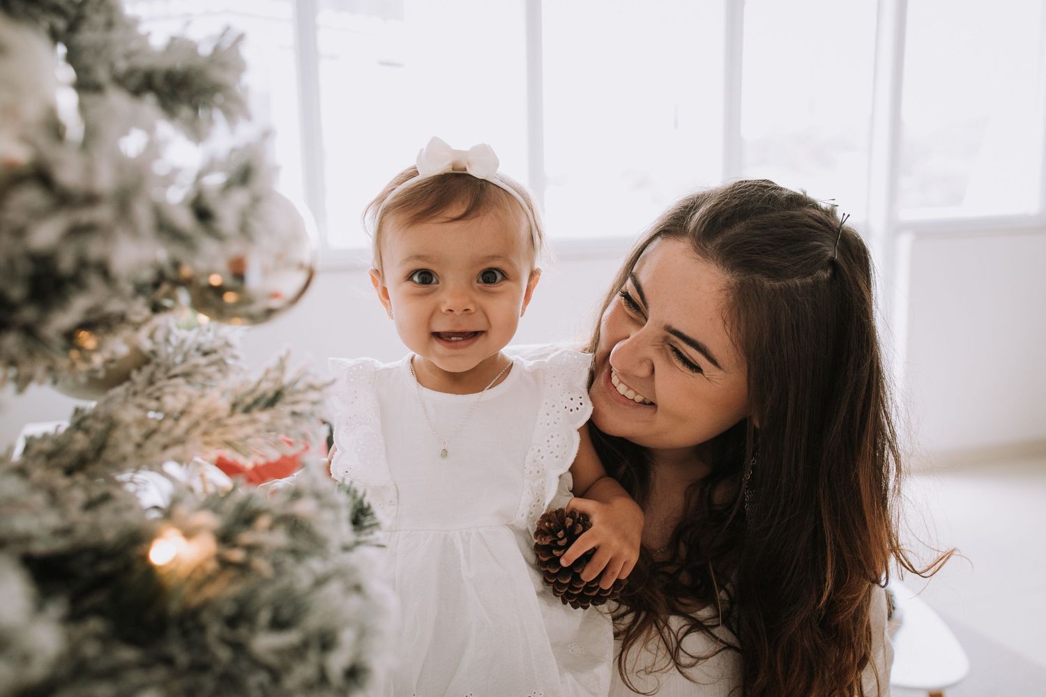 Mother and baby daughter sharing joyful moment by decorated Christmas tree.